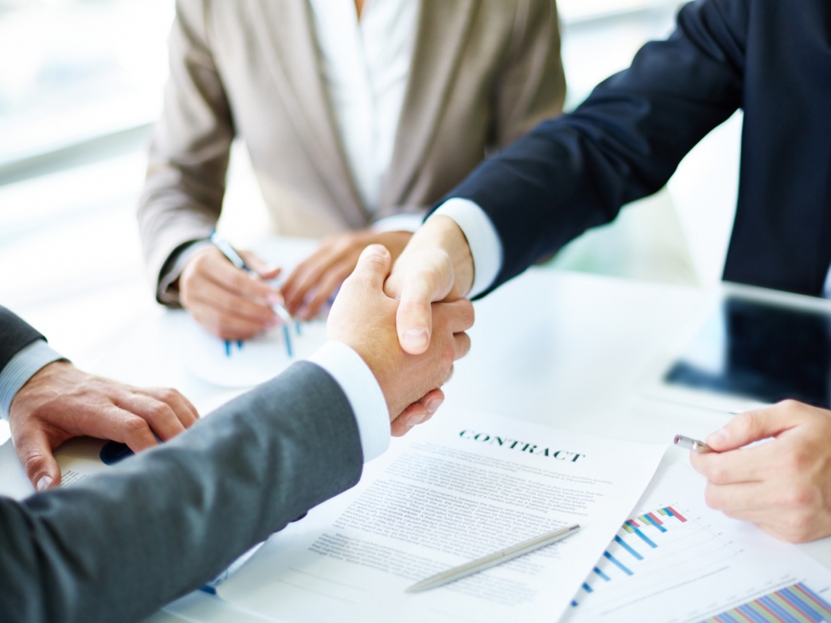 Making agreement Image of business partners handshaking over business objects on workplace